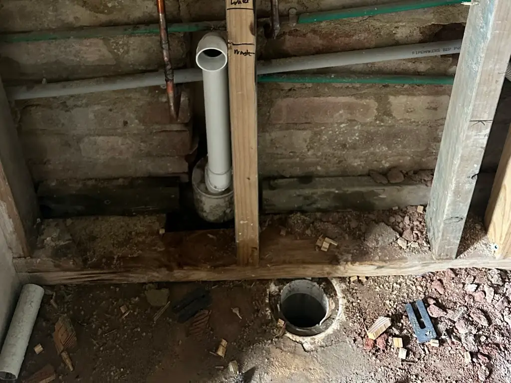 Gloved hands repairing a burst copper pipe inside an opened wall cavity under work-light at night