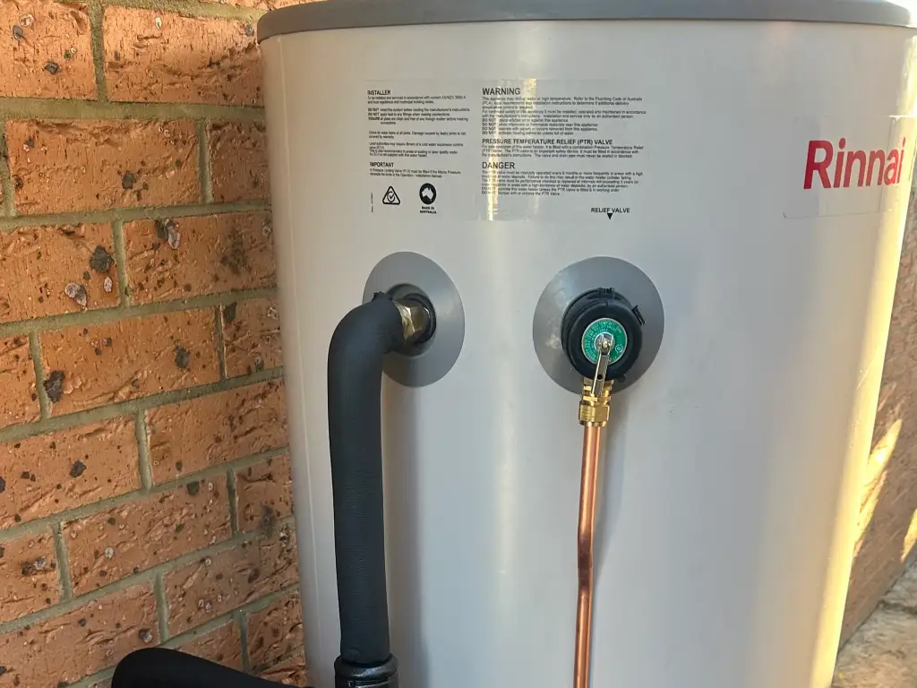 Copper pipework and brass valves beneath a new continuous-flow hot water unit on a brick wall