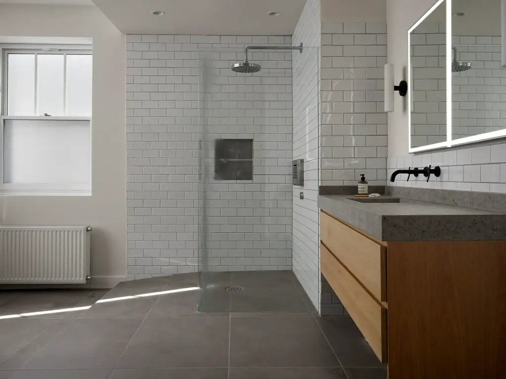 Finished bathroom renovation with subway-tiled walls, walk-in glass shower and a timber vanity with stone benchtop